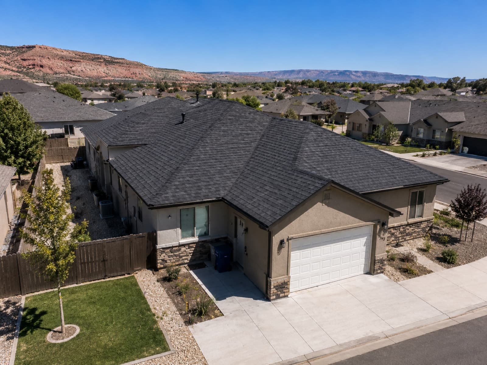 Aerial view of a completed charcoal shingle roof on a Southern Utah home with red-rock mesas in the background
