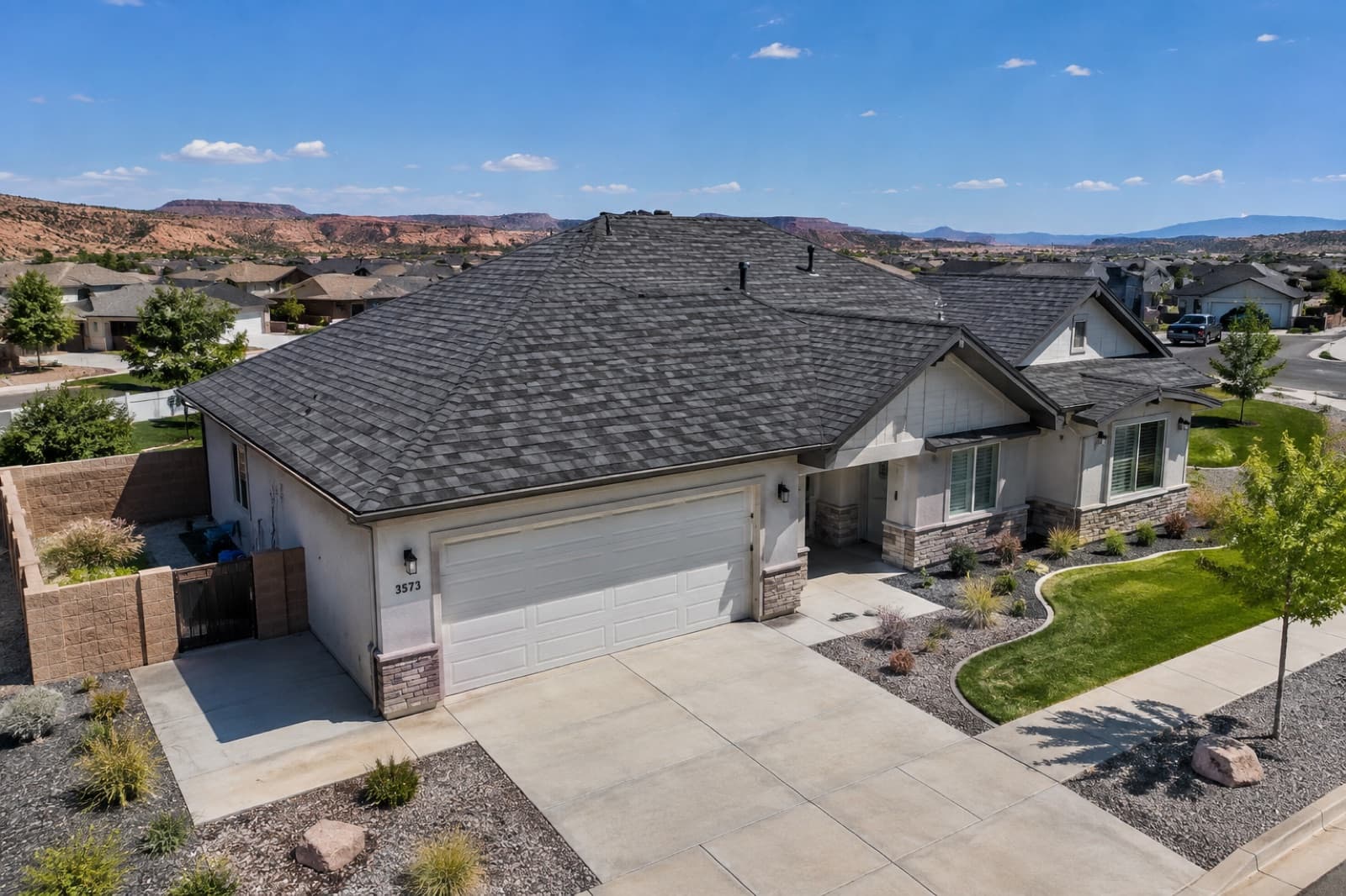 Aerial of a finished charcoal shingle roof on a Southern Utah home with red-rock mesas behind